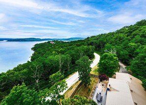 A coastal road winding through dense greenery, leading to a house with a visible deck and outdoor seating area.