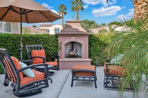 An outdoor patio with wicker chairs, a fire pit, and a large umbrella.