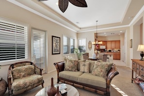 A living room with a sofa, armchair, and coffee table. There is a kitchen in the background.