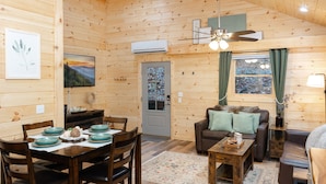 Ein Holzblockhaus-Innenraum mit Esstisch, Stühlen, einer Couch und einem Deckenventilator.