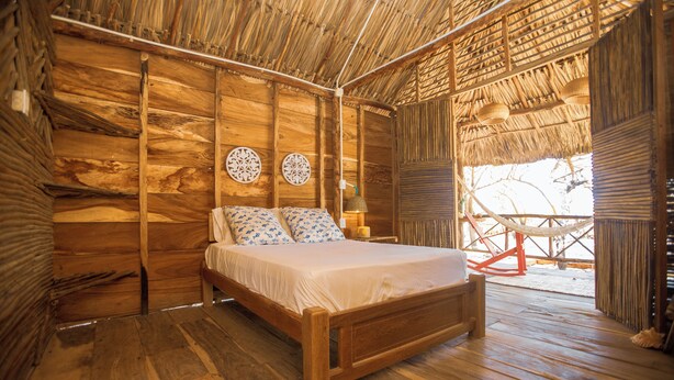 A wooden room with a bed, two wall decorations, and a thatched roof. - Morena Beach (Moñitos)