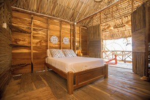 Una habitación de madera con una cama, dos adornos en la pared y un techo de paja.