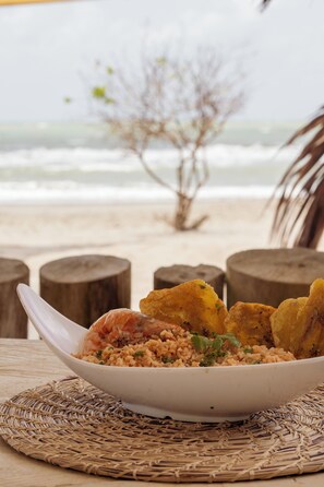 Un plato de arroz y camarones sobre una estera tejida, con vista a la playa y al océano.