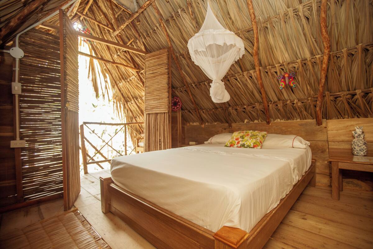 Ein Zimmer mit Strohdach, einem hölzernen Bett und einem Moskitonetz.