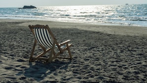 A beach with a single striped beach chair and a rocky outcrop in the water. - Morena Beach (Moñitos)