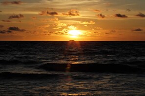 Un atardecer sobre el océano con la silueta de la costa a lo lejos.