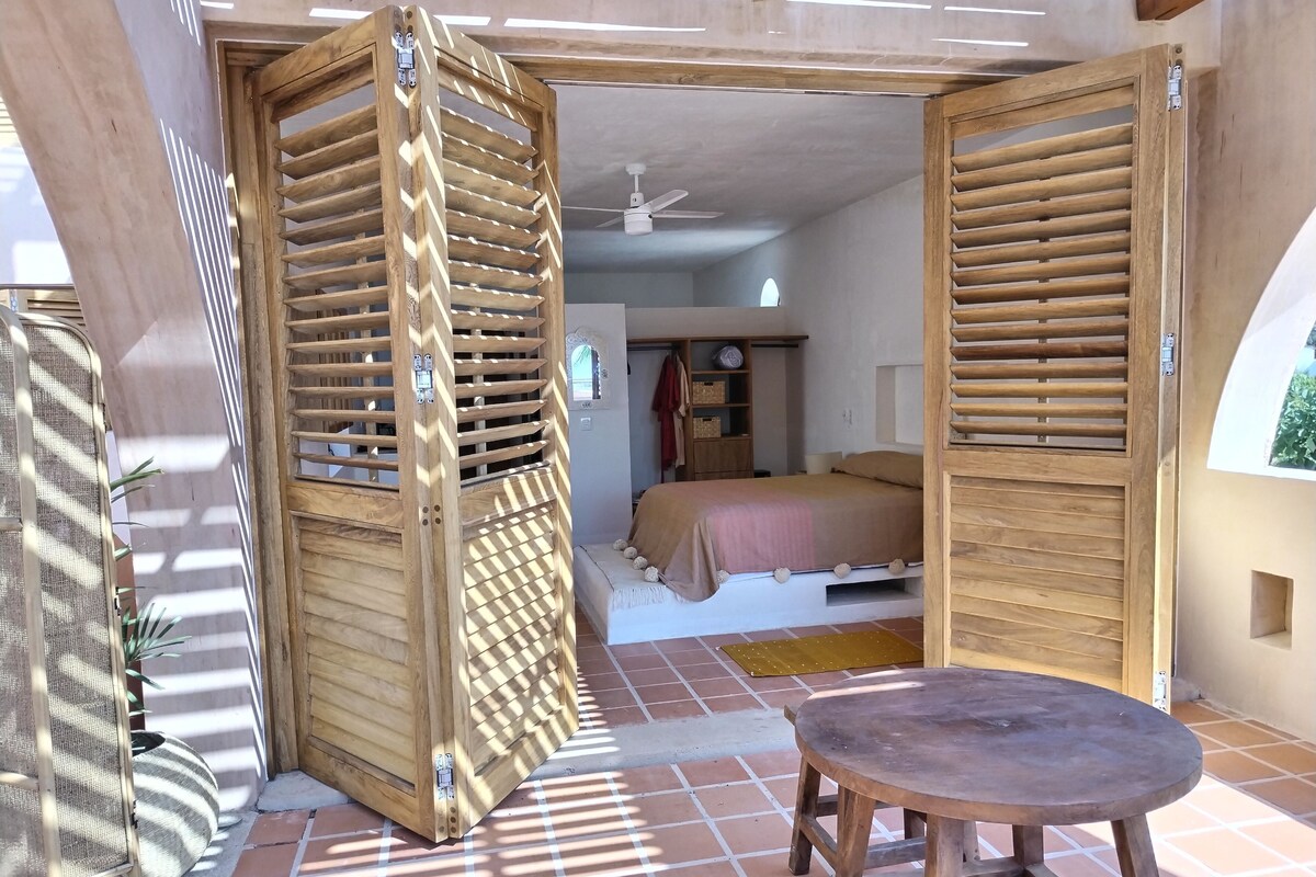 Ein Zimmer mit einem Bett, einem Holztisch und einem Fenster mit Jalousien.