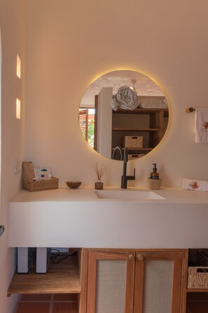Un baño con un espejo redondo, un lavabo blanco y un mueble de madera debajo.