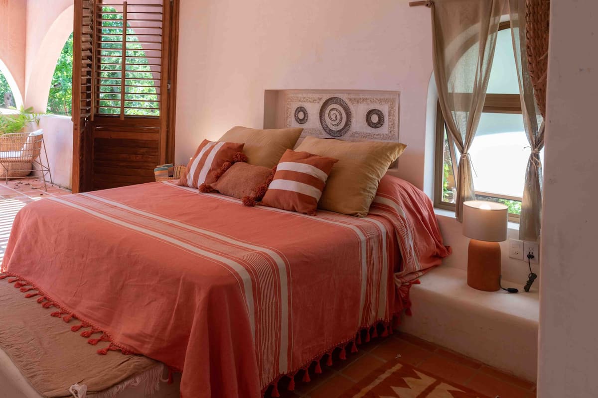 Une chambre à coucher avec un lit, une table de chevet, une lampe et une fenêtre avec des rideaux.