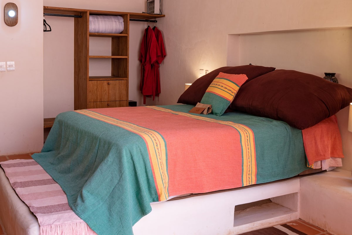 Une chambre à coucher avec un lit, un ventilateur de plafond, un appareil de climatisation, une armoire en bois et une robe rouge accrochée au mur.