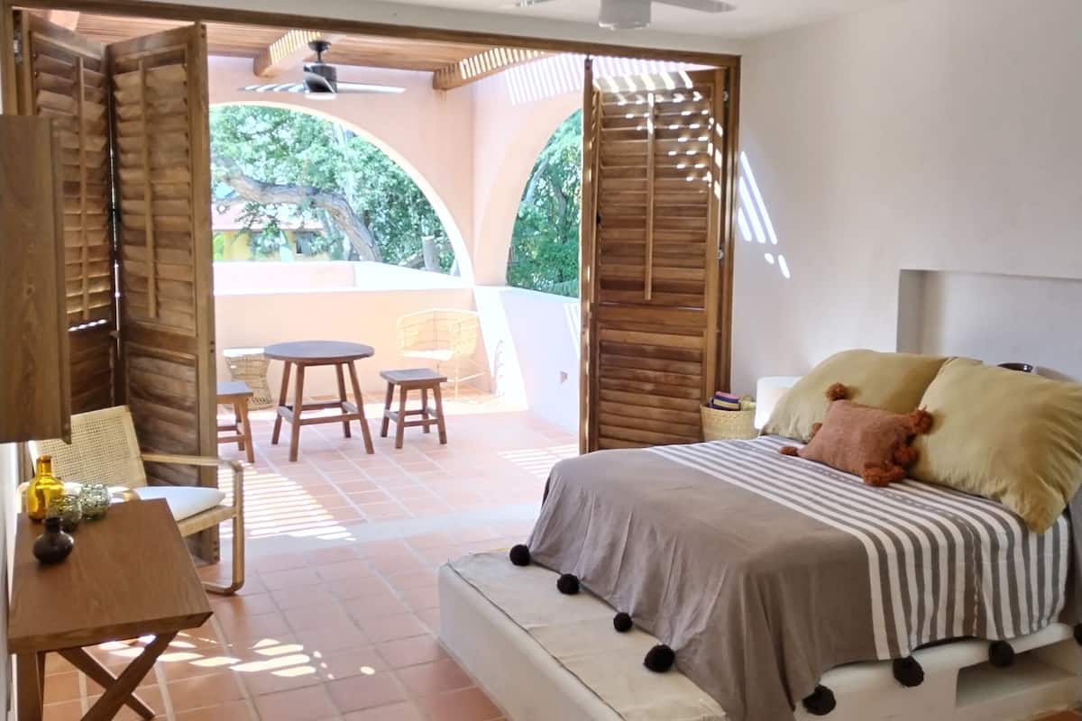 Une chambre à coucher comprenant un lit, un bureau et une chaise, un ventilateur de plafond et une vue sur l’extérieur.