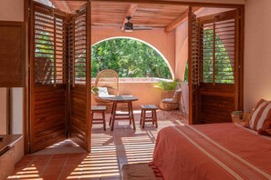 Un umbral abierto que da a un patio con una mesa, sillas, una cama y un ventilador de techo.