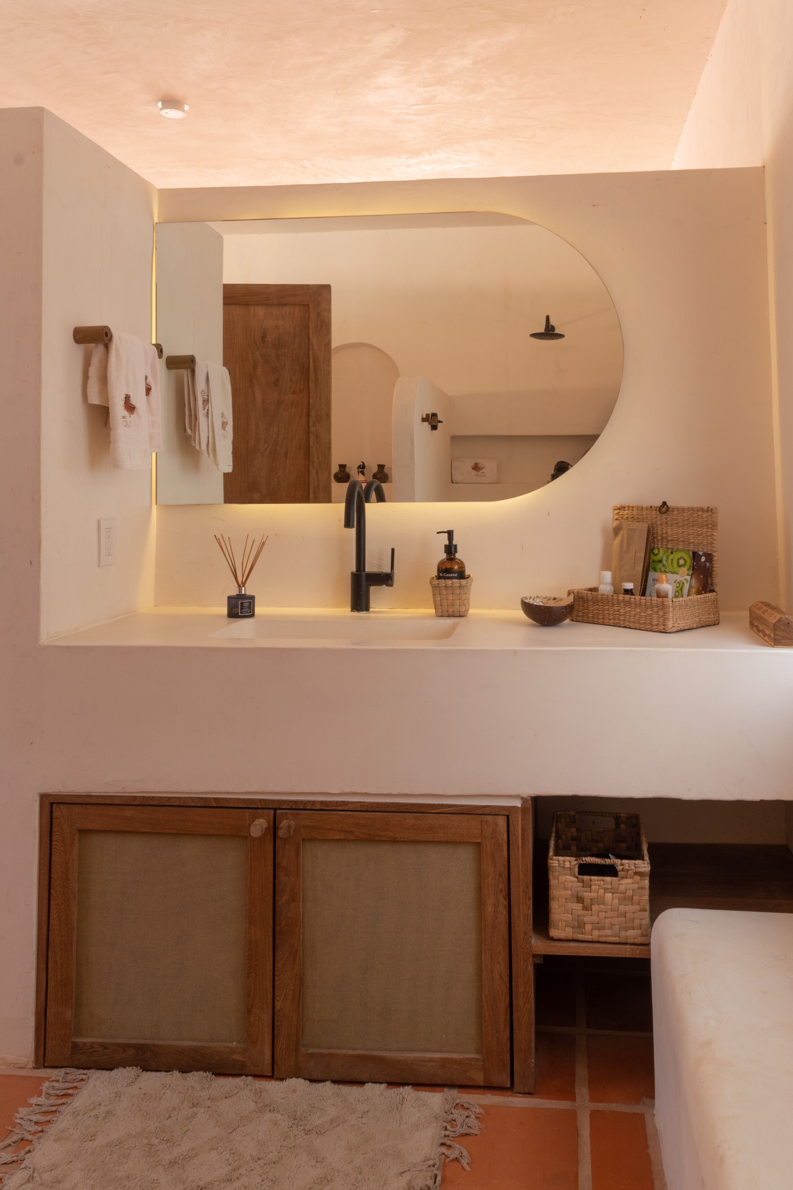 A modern bathroom with a large mirror, a sink with a soap dispenser, and a small shelf with toiletries.