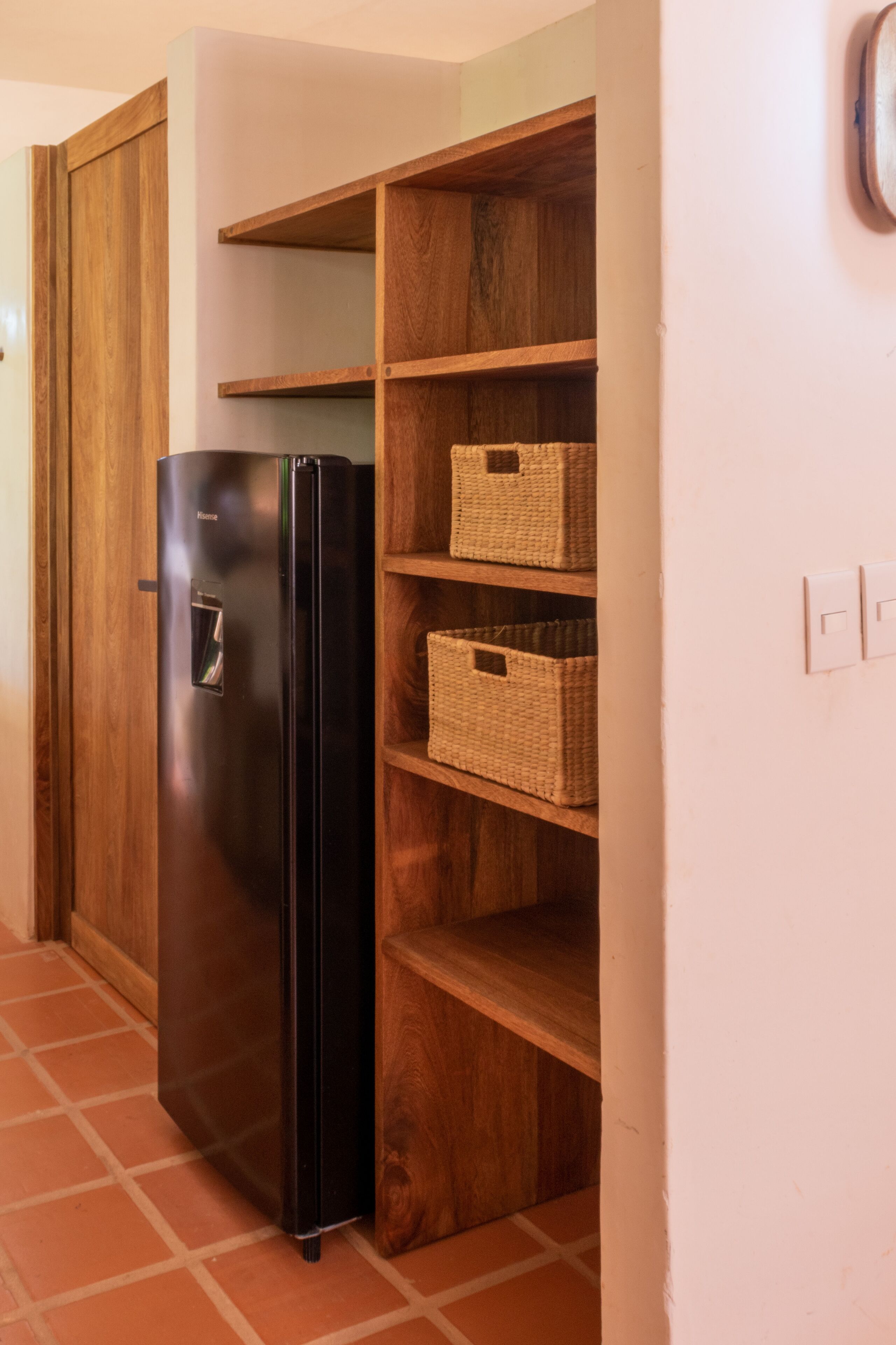 A kitchen with a black refrigerator, wooden shelves, and woven baskets.