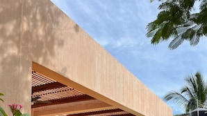 Un área de estar exterior moderna con piscina, rodeada de follaje y arcos arquitectónicos.