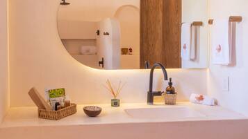 Une salle de bain moderne avec un miroir rond, un lavabo blanc, un meuble en bois et un porte-serviettes.