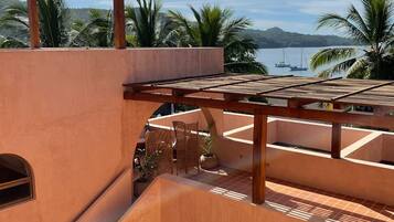 A modern outdoor patio with a wooden pergola, a curved staircase, and a view of the ocean with boats.