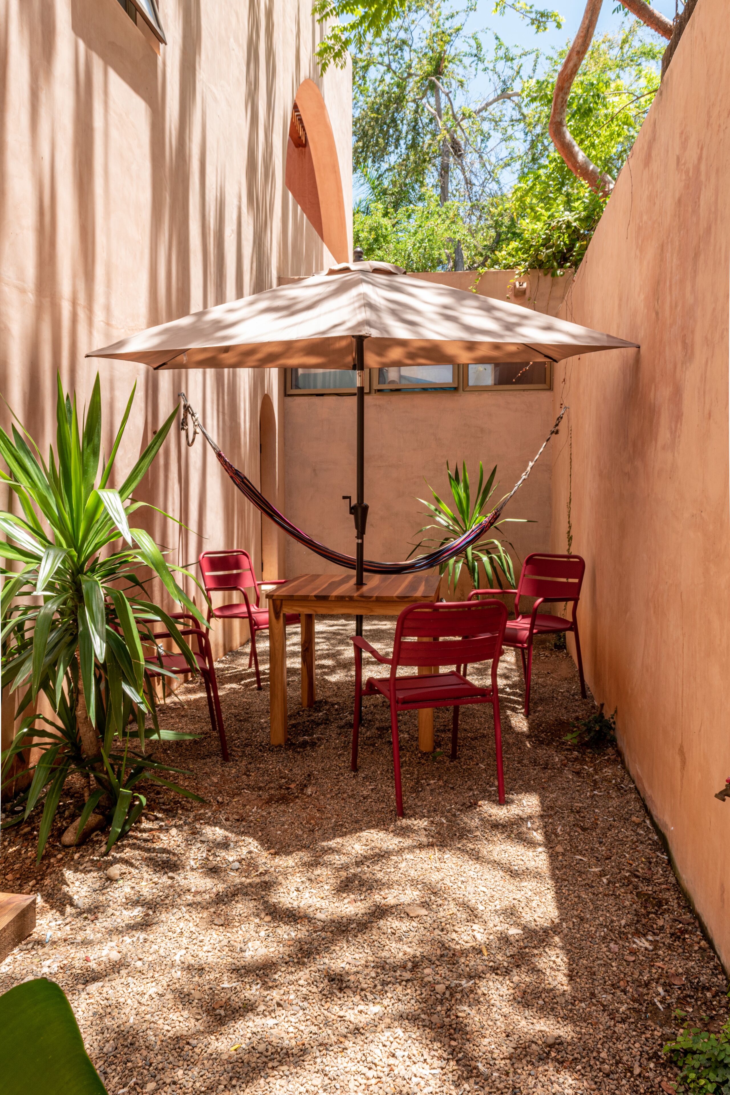 Un patio con una mesa, sillas, una hamaca y plantas en macetas.