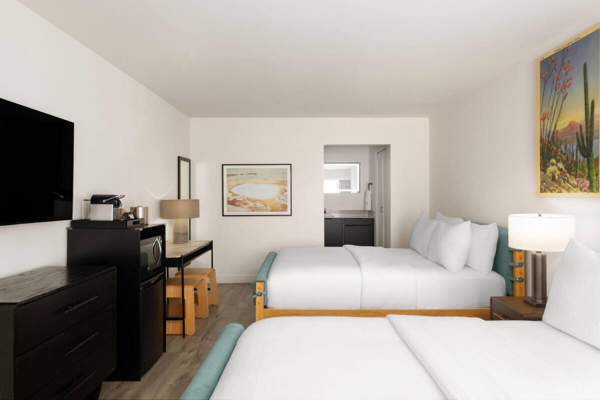 A hotel room with a bed, a desk with a lamp, a TV, and a painting on the wall.