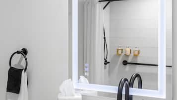 A bathroom with a white sink, a mirror with a light, a towel ring, and a shower curtain.