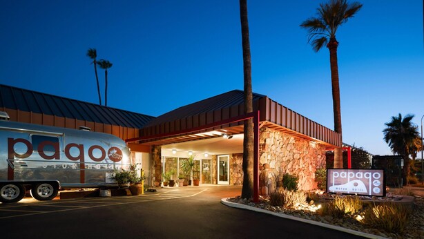 A motor hotel with a stone facade, palm trees, and a parked RV. - Papago Scottsdale by Reside, Trademark Collection by Wyndham (Scottsdale)