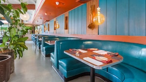 A restaurant with teal booths and wooden tables, featuring pendant lighting and potted plants.