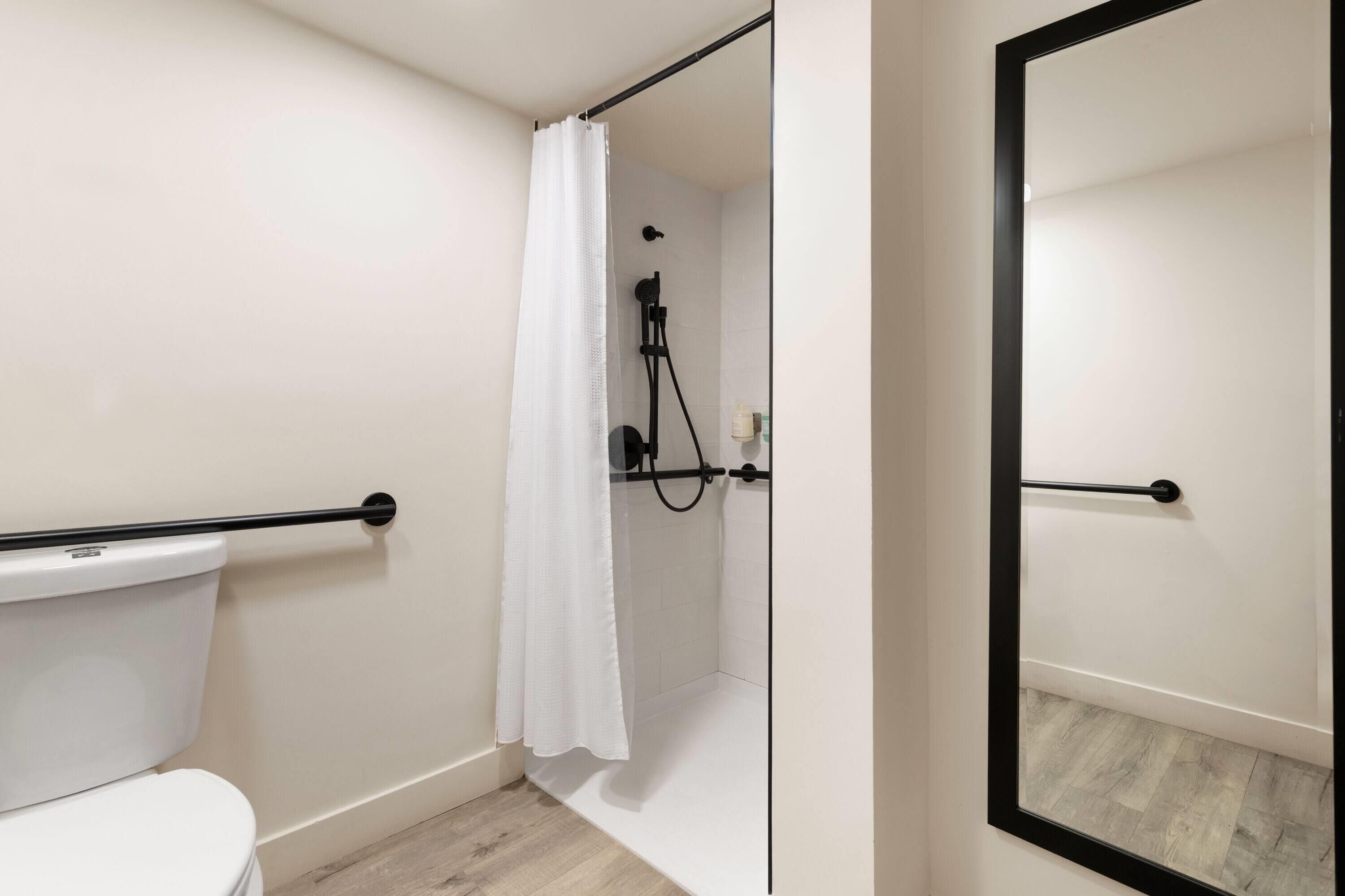 A bathroom with a white toilet, a shower with a black frame, and a mirror with a black frame.