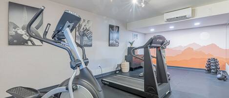 A gym with exercise equipment, including an elliptical and a treadmill, and a wall with artwork.