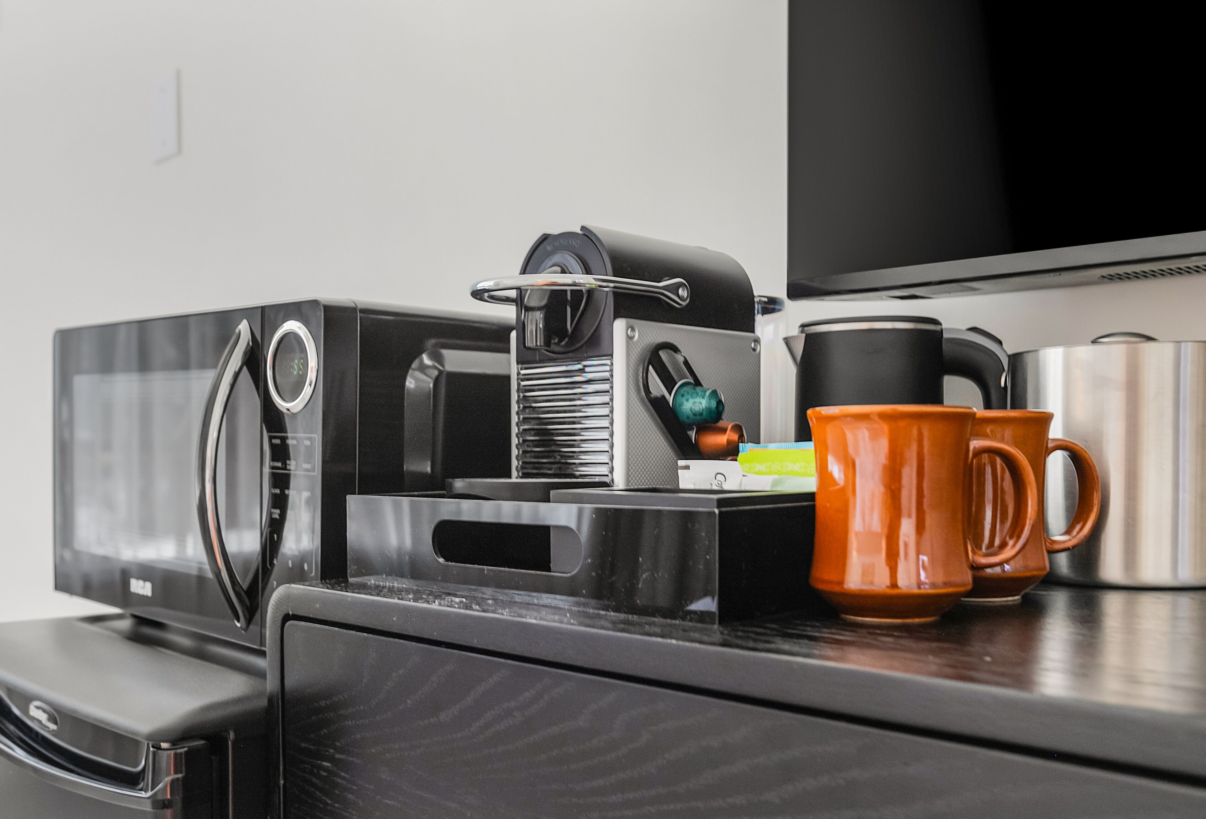 A kitchen area with a microwave, coffee maker, and orange mugs on the counter.