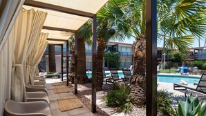 A poolside area with lounge chairs, a pool, palm trees, and a covered seating area with curtains. - Papago Scottsdale by Reside, Trademark Collection by Wyndham (Scottsdale)