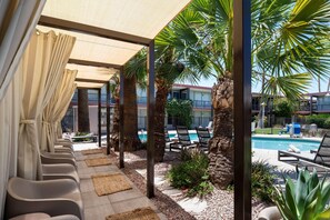 A poolside area with lounge chairs, a pool, palm trees, and a covered seating area with curtains. - Papago Scottsdale by Reside, Trademark Collection by Wyndham (Scottsdale)