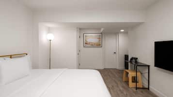 Una habitación de hotel moderna con una cama grande, un escritorio con una silla, un televisor de pantalla plana y un cuadro en la pared.