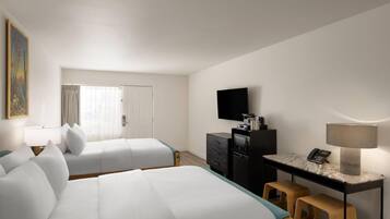 A hotel room with two beds, a desk with a lamp, a television, and a small stool.