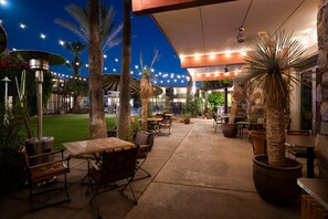 An outdoor patio area with tables and chairs, surrounded by potted plants and palm trees. - Papago Scottsdale by Reside, Trademark Collection by Wyndham (Scottsdale)