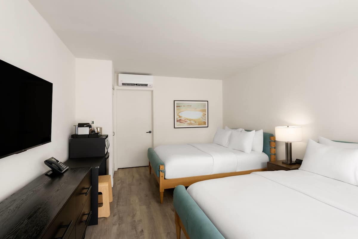 A hotel room with two beds, a desk with a phone, a TV, and a painting on the wall.
