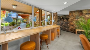 A modern bar area with a long counter, multiple stools, and large windows offering a view of the outdoor garden.