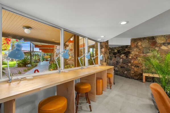 A modern bar area with a long counter, multiple stools, and large windows offering a view of the outdoor garden. - Papago Scottsdale by Reside, Trademark Collection by Wyndham (Scottsdale)