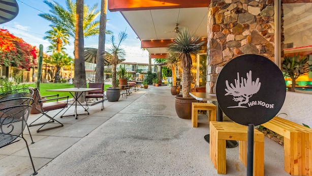 An outdoor patio area with tables and chairs, surrounded by potted plants and palm trees.