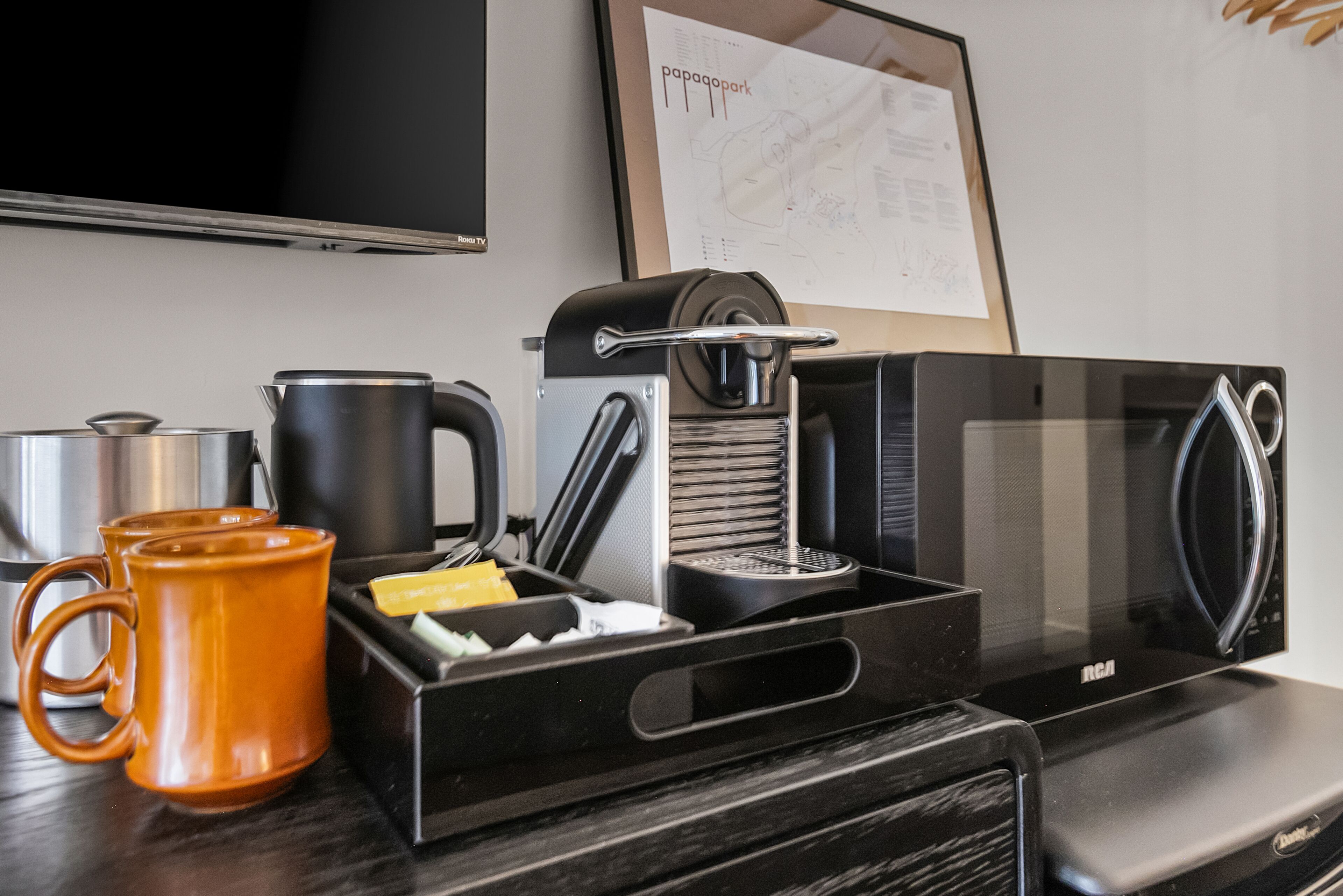 Un coin cuisine comprenant une machine à café, une bouilloire et deux tasses oranges posées sur un plan de travail.
