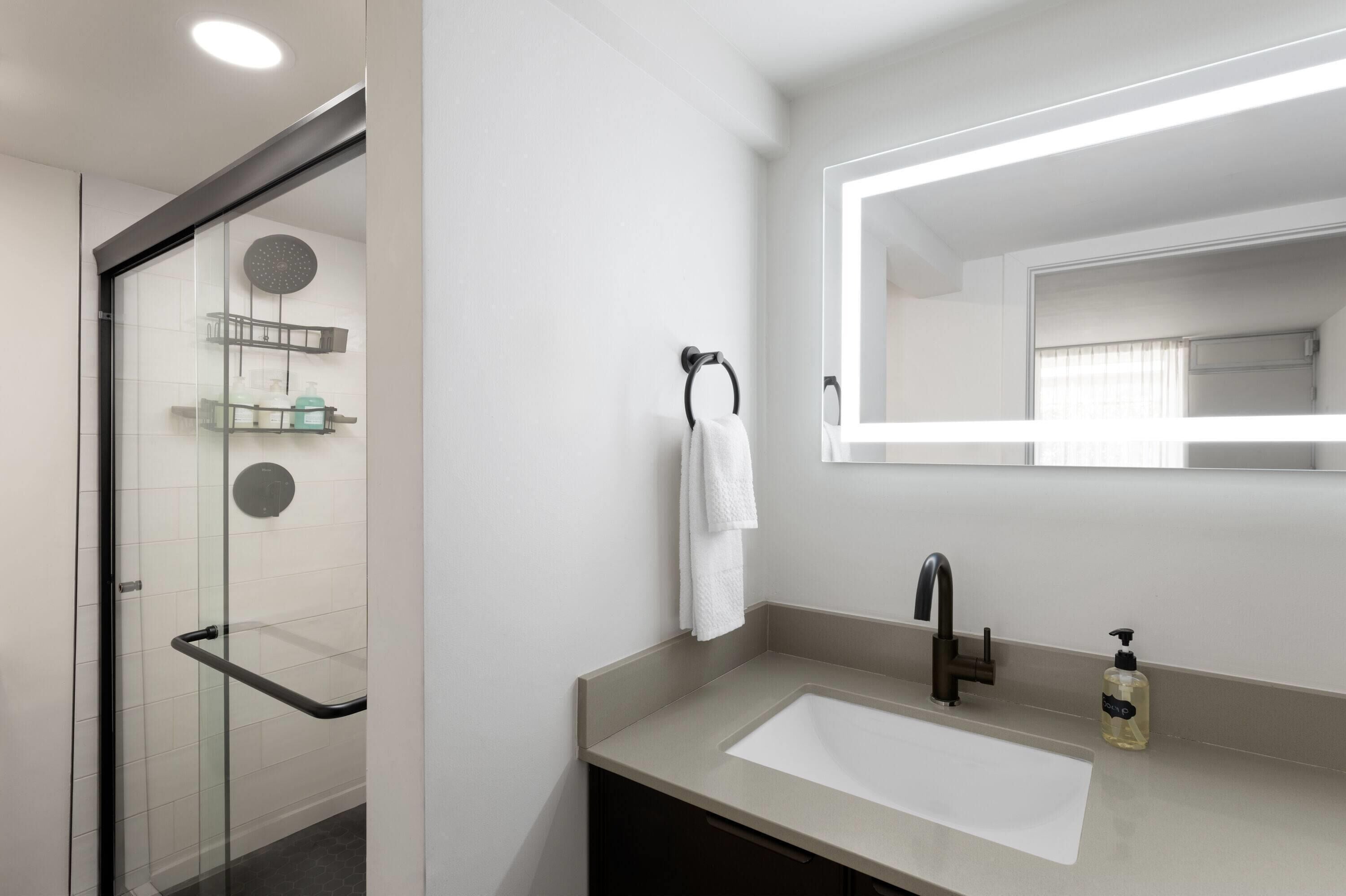 Un baño moderno con cabina de ducha de vidrio, un espejo grande y un lavabo con grifo.