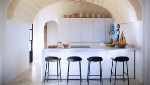 A modern kitchen with a central island, three black bar stools, and a rustic ceiling.