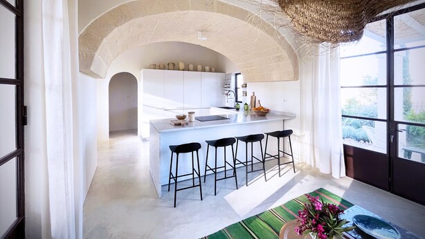 A modern kitchen with an island, bar stools, and a view of the outdoors.