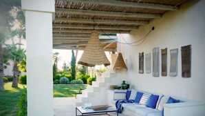 A covered outdoor seating area with a white sofa, a coffee table, and hanging woven light fixtures.