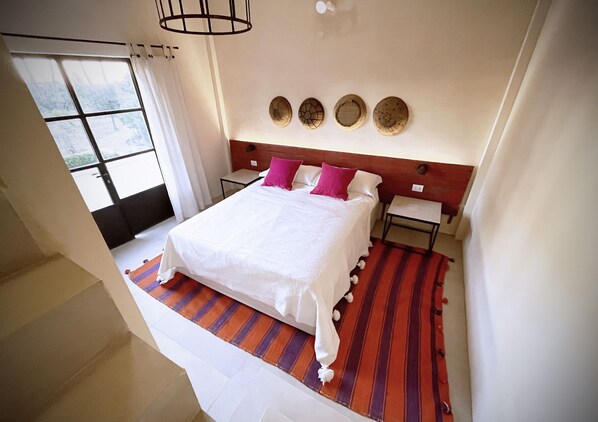 Una habitación de hotel con una cama grande, dos almohadas, un felpudo a rayas y una ventana con cortinas.