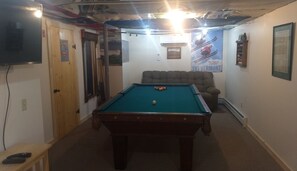 A pool table in a room with a ceiling fan, a couch, and a poster of a skier. - Beautiful Vermont Farmhouse with views of Mount Mansfield (Cambridge)
