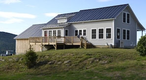 A two-story house with a metal roof, a wooden deck, and a garage. - Beautiful Vermont Farmhouse with views of Mount Mansfield (Cambridge)