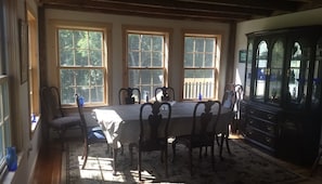 A dining room with a table set for six, large windows, and a dark wooden cabinet. - Beautiful Vermont Farmhouse with views of Mount Mansfield (Cambridge)