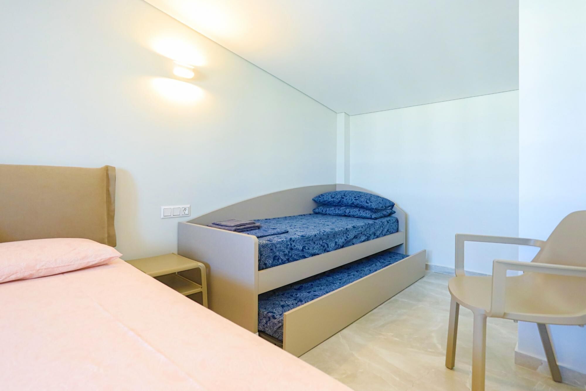 Ein kleines Schlafzimmer mit Etagenbett, einem Einzelbett, einem Stuhl und einem kleinen Tisch.