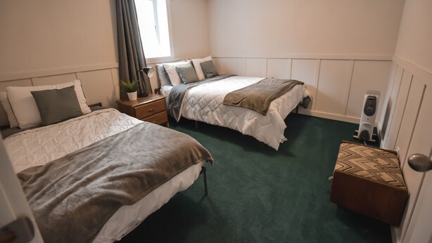 Een kamer met twee bedden, een tafeltje, een plant in pot en een radiator.