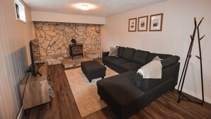 Een woonkamer met een stenen openhaard, een zwarte bank, een poef en een houten tv-meubel.